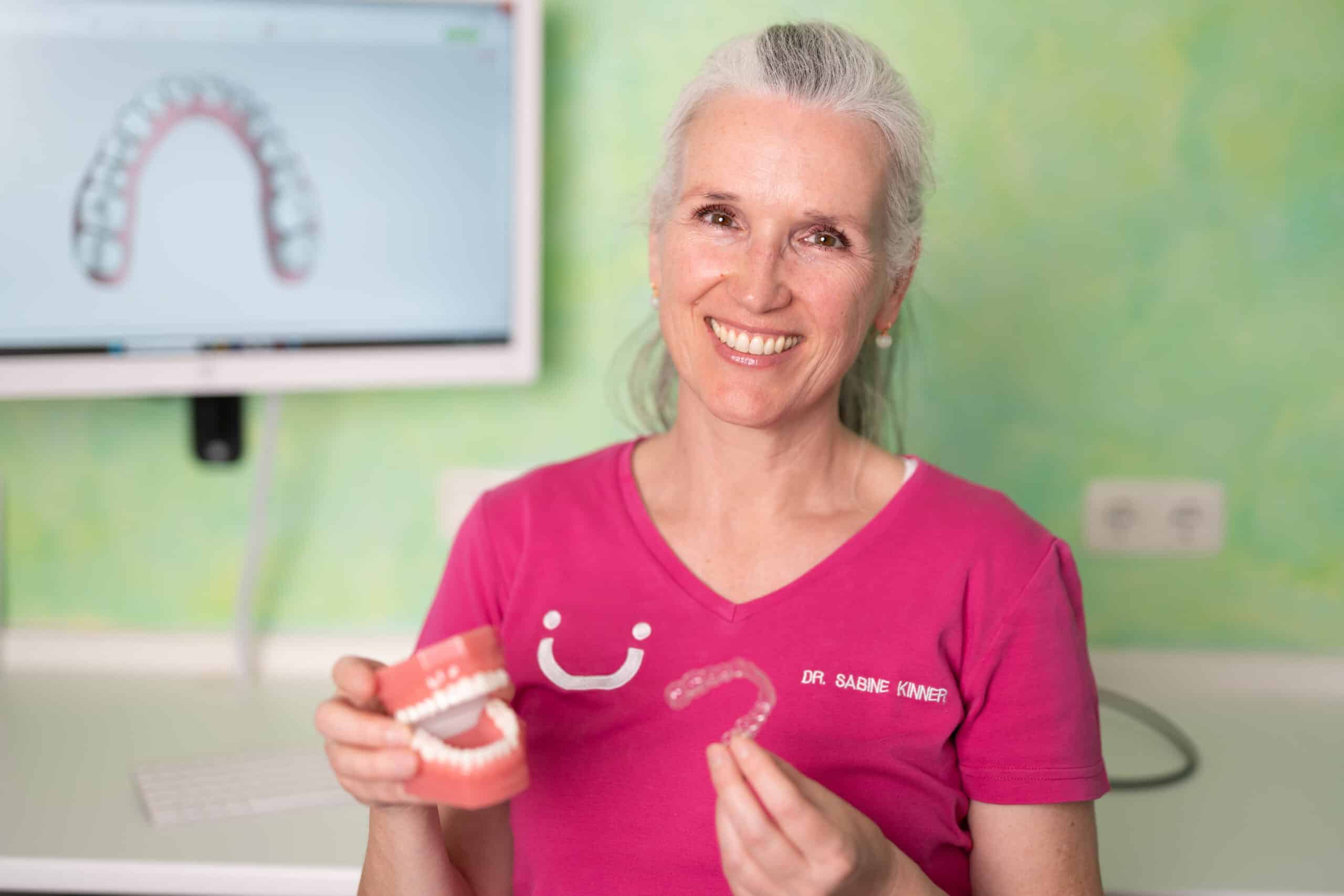 Dr. Sabine Kinner hält einen Aligner und ein Gebiss in ihrer Praxis